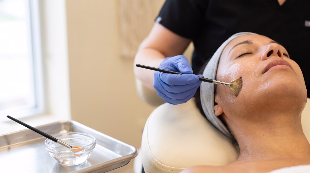 A fan brush painting a thin layer of clear peel solution across a cheek