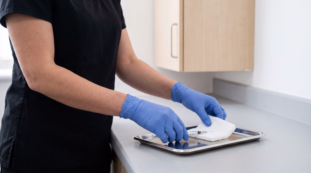 Gloved hands laying a prepared syringe and folded gauze on a steel tray before treatment