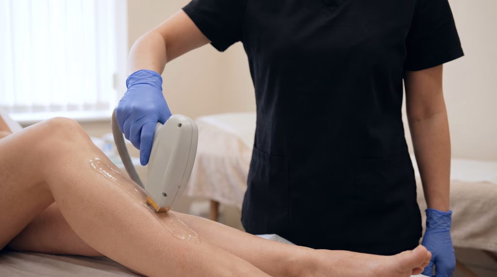 A laser hair removal handpiece drawn in a line down a woman's lower leg with gel ahead of it