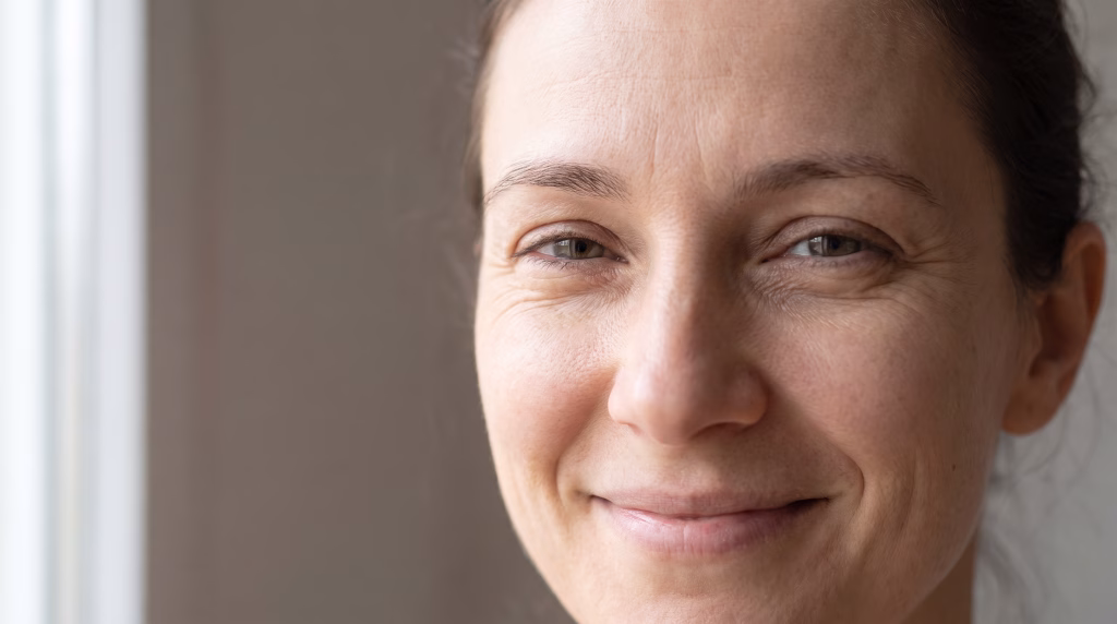 A woman smiling naturally with clear movement in the brow and fine lines at the outer eye